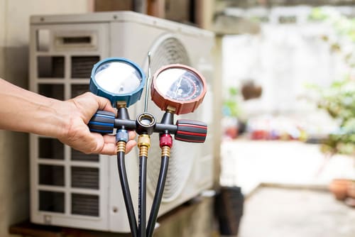 a maintenance worker’s hands holding up a gauge connected to a heating system