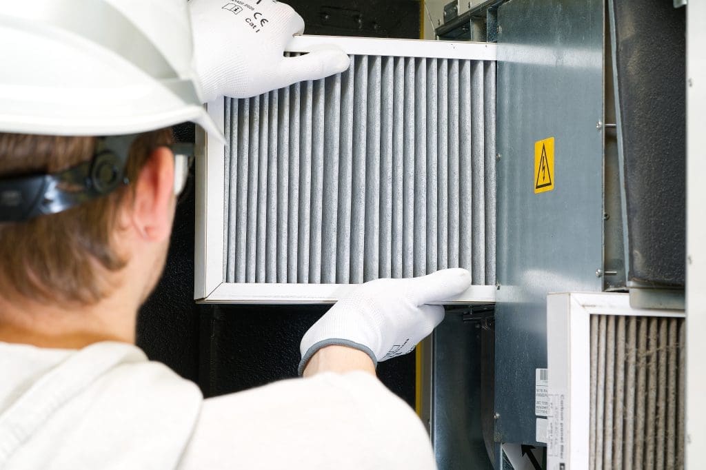 A maintenance worker checking an air filter in an indoor heating unit.